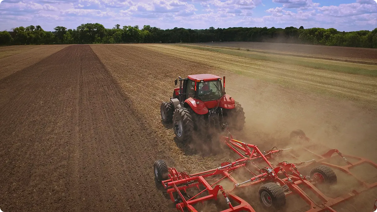 Tractor tilling a field, dust rising behind it in an agricultural setting.