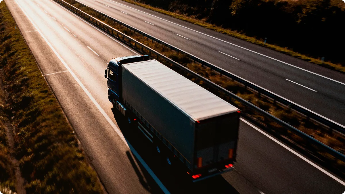 Truck driving on a highway at sunset, seen from above.